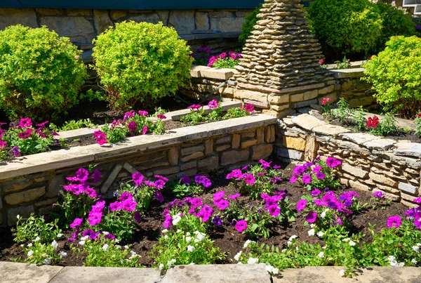 Landscape design of home garden, landscaping with flowers and stone retaining walls in house backyard in summer. Beautiful flowerbed and trimmed plants in landscaped yard.