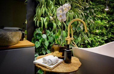 Luxury bathroom interior in spa with vertical garden, bath in modern beauty salon. Green plants wall, flowers and bathtub in hotel. Concept of nature, landscaping, water, wellness, room.