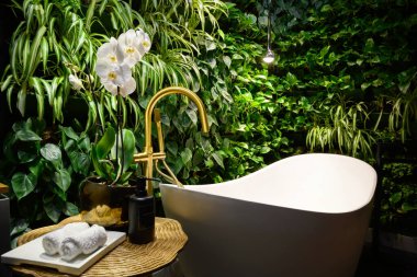 Bath in modern beauty salon, luxury bathroom interior in spa with vertical garden. Green plants wall, flowers and bathtub in hotel. Concept of nature, landscaping, water, wellness, room.
