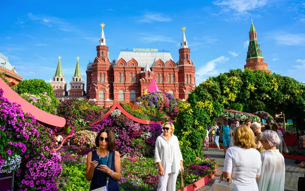 Moscow - Aug 2, 2022: Festival of flowers on Manezhnaya Square, Moscow, Russia. Historical Museum and Kremlin, tourist attractions in distance. People walk by floral decorations in Moscow city center