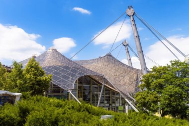 Yaz mevsiminde Olimpiyat parkında cam gerilim çatısı, Münih, Almanya. Münih 'in dönüm noktası olan stadyumun mimari tasarımının manzarası. Olympiapark 'ta inşaat manzarası.