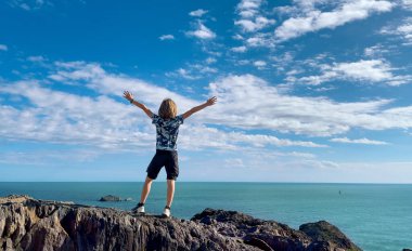 Genç çocuk kollarını kaldırıp denize bakıyor.