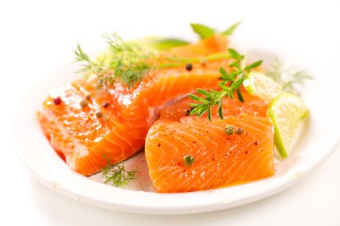 Beyaz arkaplanda çiğ somon ve bitkiler izole edilmiş.