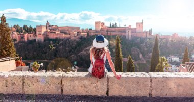 Woman sitting on wall,  enjoying beautiful panoramic view of Alhambra Granada view- Andalusia in Spain