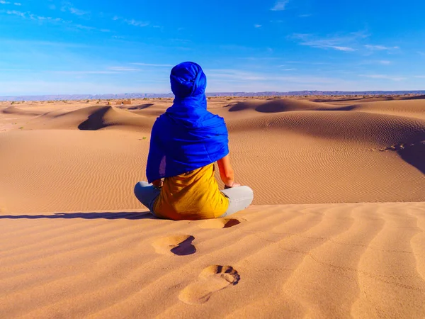 青いゴム製のターバンを持つ女性がサハラ砂漠に座って パノラマビューを見ます — ストック写真