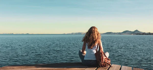 美丽的女人坐在木制码头上 凝视着海上自由 旅行的概念 — 图库照片
