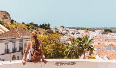 Balkonda oturan bir kadın manzaraya ve Portekiz 'deki köy manzarasına bakıyor Castro Maria Algarve.