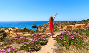 Algarve sahilinde dans eden kırmızı elbiseli güzel bir kadın. İnanılmaz çiçekleri olan Portekiz 'de turizm.