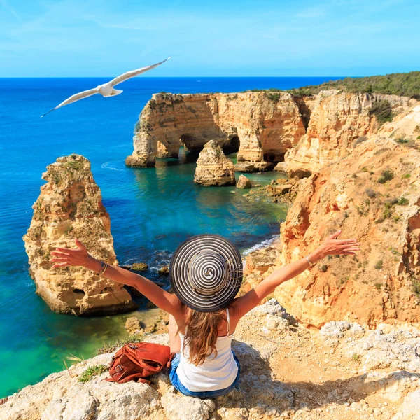 Woman tourist looking at impressive view of Algarve rock formation,  coast of the Algarve- Tourism,  travel,  vacation in Europe (natural cave or arch on praia da marinha)- Portugal