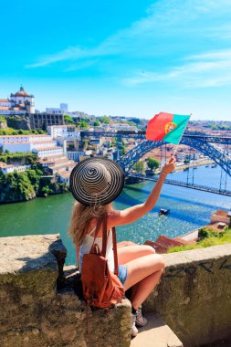 Portekiz 'de Portekiz bayrağı taşıyan ve demir köprü ve douro nehrinin panoramik tadını çıkaran bir kadın turist.