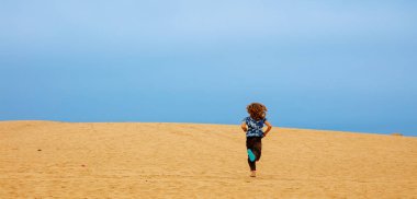 Sahra çölünde kum tepelerinde koşan genç bir çocuk.
