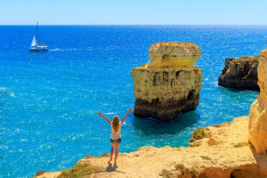 Mutlu kadın Atlantik Okyanusu 'nun güzel manzarasını, kaya oluşumunu ve tekneyi seyrediyor. Tatil, yaz tatili, seyahat yeri kavramı. Portekiz, Algarve Sahili ve Plajı.