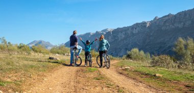 Bisikletli mutlu aile ve çocuklar bisikletle eğleniyor.