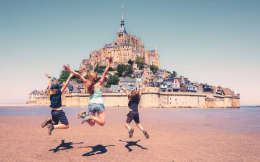 Mont Saint Michele 'in önüne atlayan mutlu bir aile. Tatil, seyahat, turizm konsepti.