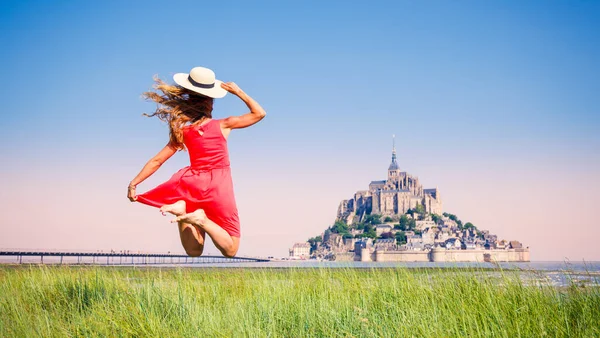 赤いドレスと帽子を持つ幸せな女性は モンサンミシェルの前でジャンプ フランスのノルマンディー — ストック写真