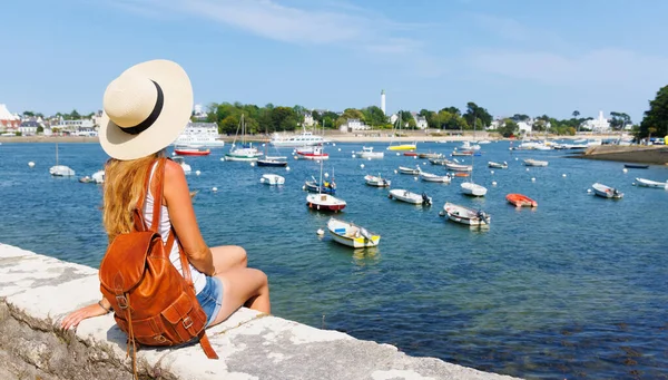 帽子とバックパックを持つ女性が座っているとボート ポートの景色を楽しんで フランスのブルターニュ — ストック写真