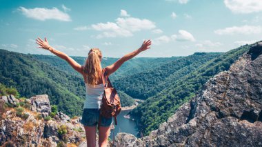 Kolları açık mutlu bir kadın nehir, dağ ve ormanın güzel manzarasının tadını çıkarıyor.