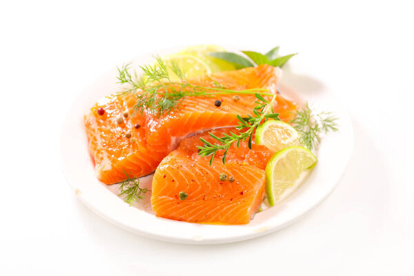 salmon fillet, lemon and herbs on plate on white background