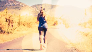 Kadın koşucu parkta güneş ışığıyla koşuyor. Spor, motivasyon.