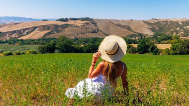 Beyaz elbiseli ve şapkalı genç bayan turist Toskana manzarasının tadını çıkarıyor- İtalya