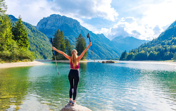 Travel and active lifestyle concept- Happy woman with arms open holding walking sticks enjoying spectacular mountain lake in Italy