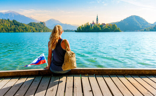 Woman tourist with Slovene flag enjoying majestic landscape view of Bled lake- tour tourism, travel, vacation in Slovenia