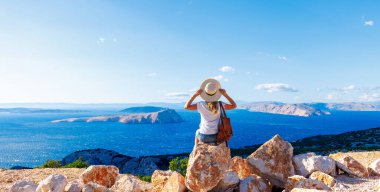 Kaya üzerinde oturan kadın deniz ve adaların panoramik manzarasının tadını çıkarıyor- seyahat, tatil, macera, turizm konsepti
