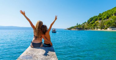 Anne ve oğlu rıhtımda oturmuş güzel denizlerin tadını çıkarıyorlar. Seyahat, tatil, tropikal tatil beldesi.