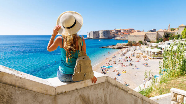 Женщина турист с сумкой и шляпой глядя на город Дубровник в Хорватии - путешествия, туристический туризм, отдых в Европе