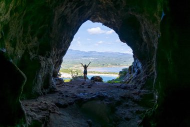 Mağaradaki kadının silueti denizin panoramik manzarasının tadını çıkarıyor.