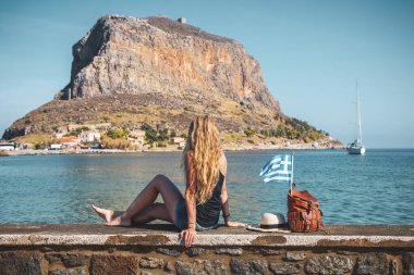 Çantalı, şapkalı ve Yunan bayrağıyla seyahat eden genç bir turist. Seyahat, tatil veya turizm konsepti.