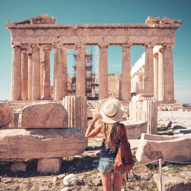 Atina 'da seyahat yeri şapka ve çantalı genç bir kadın turist Akropolis, Yunanistan' daki eski harabe tapınağına bakıyor.
