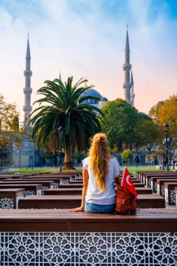 Kürsüde oturan kadın turist Mavi camiye ve palmiye ağacına bakıyor, İstanbul, Türkiye