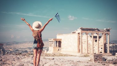 Atina, Akropolis 'te şapka, çanta ve Yunan bayrağıyla gezgin genç bayan