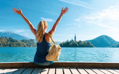 Slovenya ve Bled gölü üzerinde tahta iskelede oturan genç bir kadın seyahat, özgürlük, macera