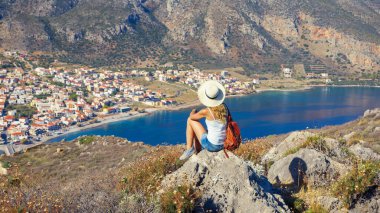 Uçurumda oturan genç kadın, Yunan şehri Mora 'nın panoramik manzarasına bakıyor.