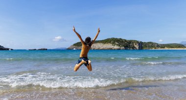 Genç bir çocuk sahilde zıplıyor. Mutlu yaz tatilleri.