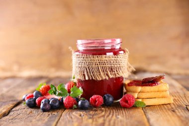 Bir kavanoz meyve reçeli ve ahşap arka planda bisküvi.