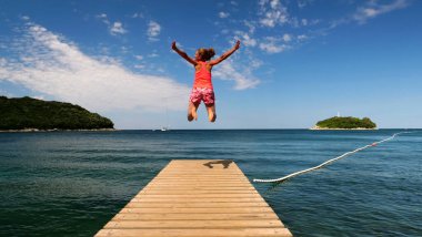 Mutlu kadın ahşap iskelede zıplıyor. Deniz tatilinin, seyahat yerinin, yaz konseptinin tadını çıkarıyor.