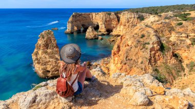 Porugal 'daki Algarve' de kayalıklı plajların panoramik manzarasından hoşlanan güzel bir kadın.