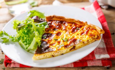 Bir dilim Quiche Lorraine 'in tabağında salata ve çatalla en iyi görüntüsü yumurtalı, pastırmalı ve peynirli lezzetli bir Fransız yemeği, taze, sağlıklı bir salata ile servis edilir.