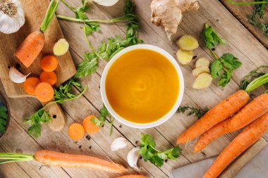 Ahşap zemin üzerinde havuç, ot ve zencefil olan sebze çorbası kasesinin üst görüntüsü. Sağlıklı beslenme ve mevsimsel yemek kavramları için mükemmel.