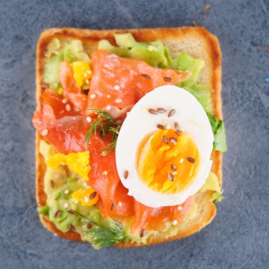 Avokado, tütsülenmiş somon ve yumurtalı tost manzarası. Sağlıklı kahvaltı ve gurme yemek fikirleri için mükemmel.