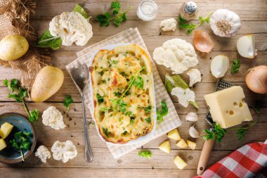 Ahşap zemin üzerinde malzemeler olan fırında pişmiş karnabahar graten manzarası. Sağlıklı yemekler ve konfor sunumları için ideal.