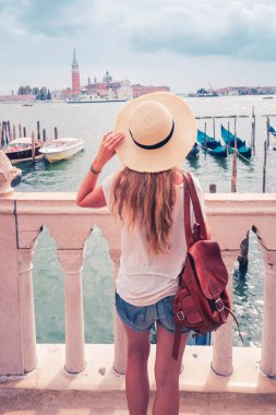 İtalya 'nın Venedik kentindeki geleneksel gondola bakan şapkalı ve çantalı genç bir turist.