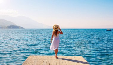 Beyaz elbiseli ve şapkalı genç bir kadının denize bakışı. Özgürlük, tasasız, huzur, seyahat