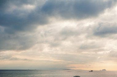 Dramatik gökyüzü, deniz suyu, gemi ve adaları olan güzel bir manzara.