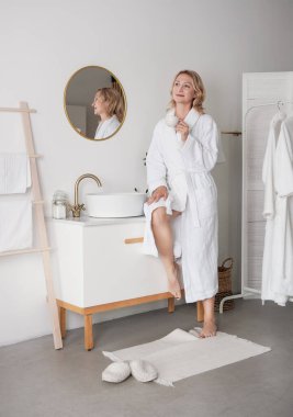 Güzel, yetişkin bir kadın banyoda uzun bir bornoz giyiyor ve kahve içiyor.