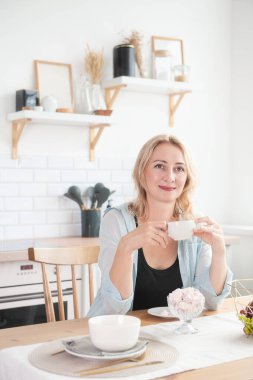 Mutfakta bir fincan kahveyle sandalyede oturan mutlu güzel kadın.