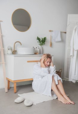 Üzgün, uzun bornoz giymiş güzel bir kadın banyoda yerde oturmuş ağlıyordu.